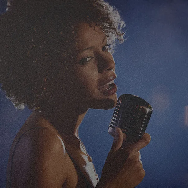 A photo of a black women who is holding a mike. The tone is dark blue with low saturation and grainy texture over it.